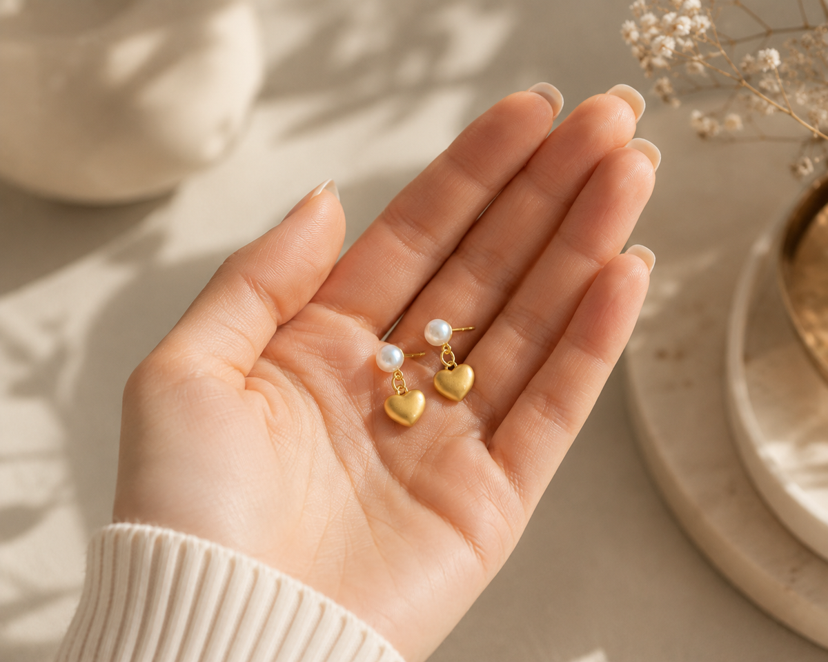 Pair of freshwater pearl heart drop earrings displayed in a hand