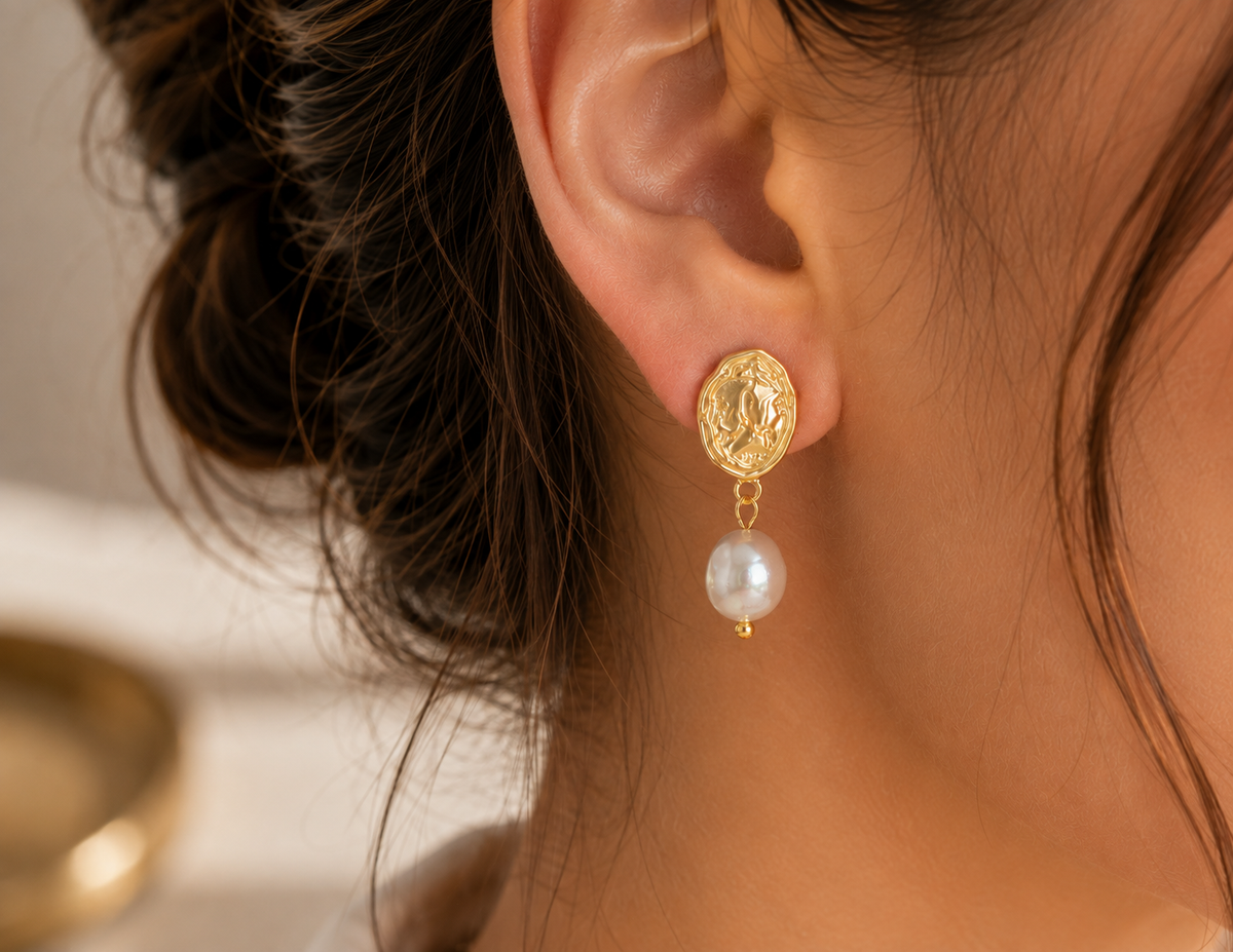 Detailed view of a freshwater pearl drop earring with an embossed gold-tone medallion