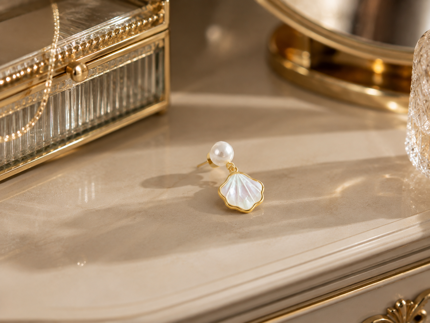 Freshwater pearl shell drop earring displayed on a cream vanity beside a glass jewelry box