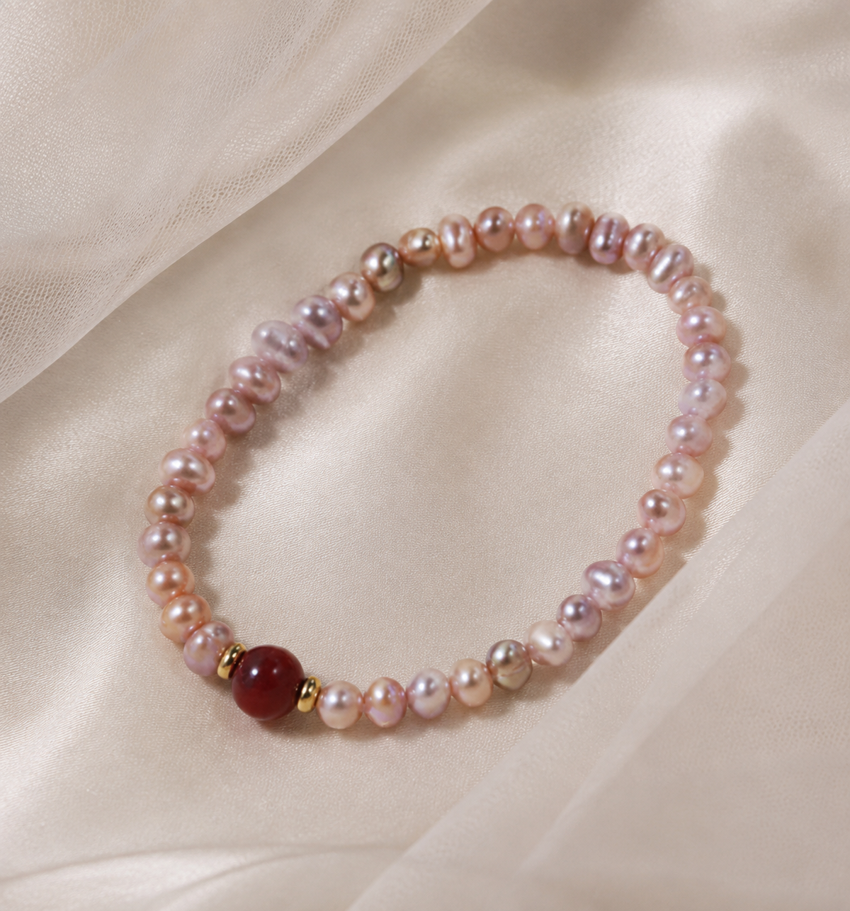 Close-up of a red center stone, gold tone spacers, and pink freshwater pearls