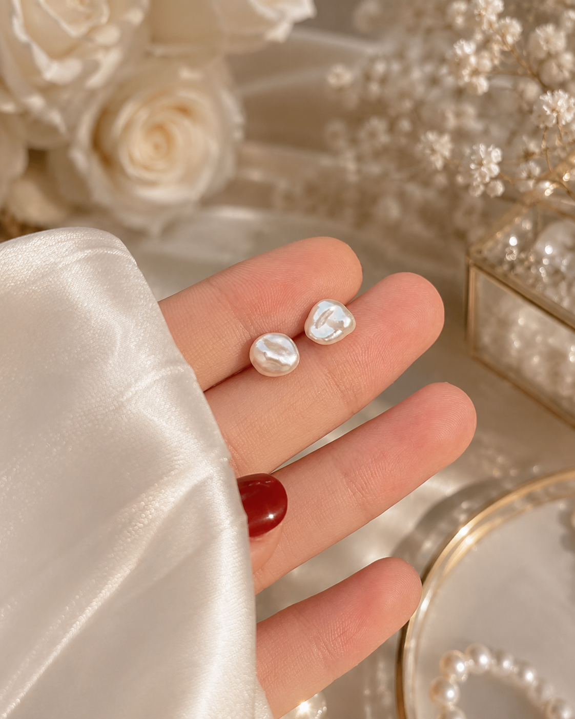 Pair of white baroque freshwater pearl stud earrings displayed in hand