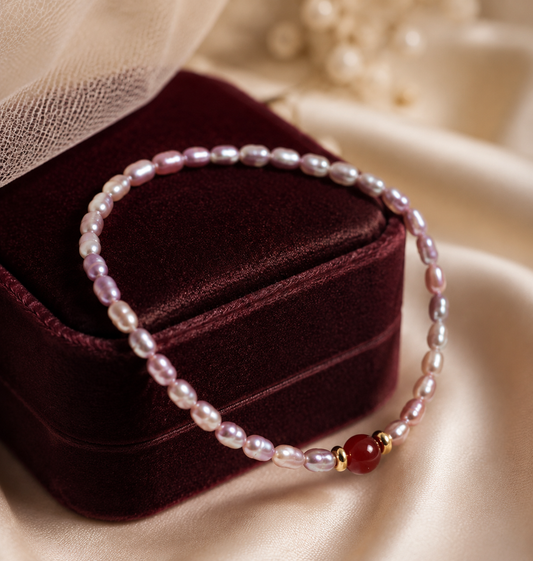 Delicate pink rice pearl bracelet with a red center stone and gold tone spacers