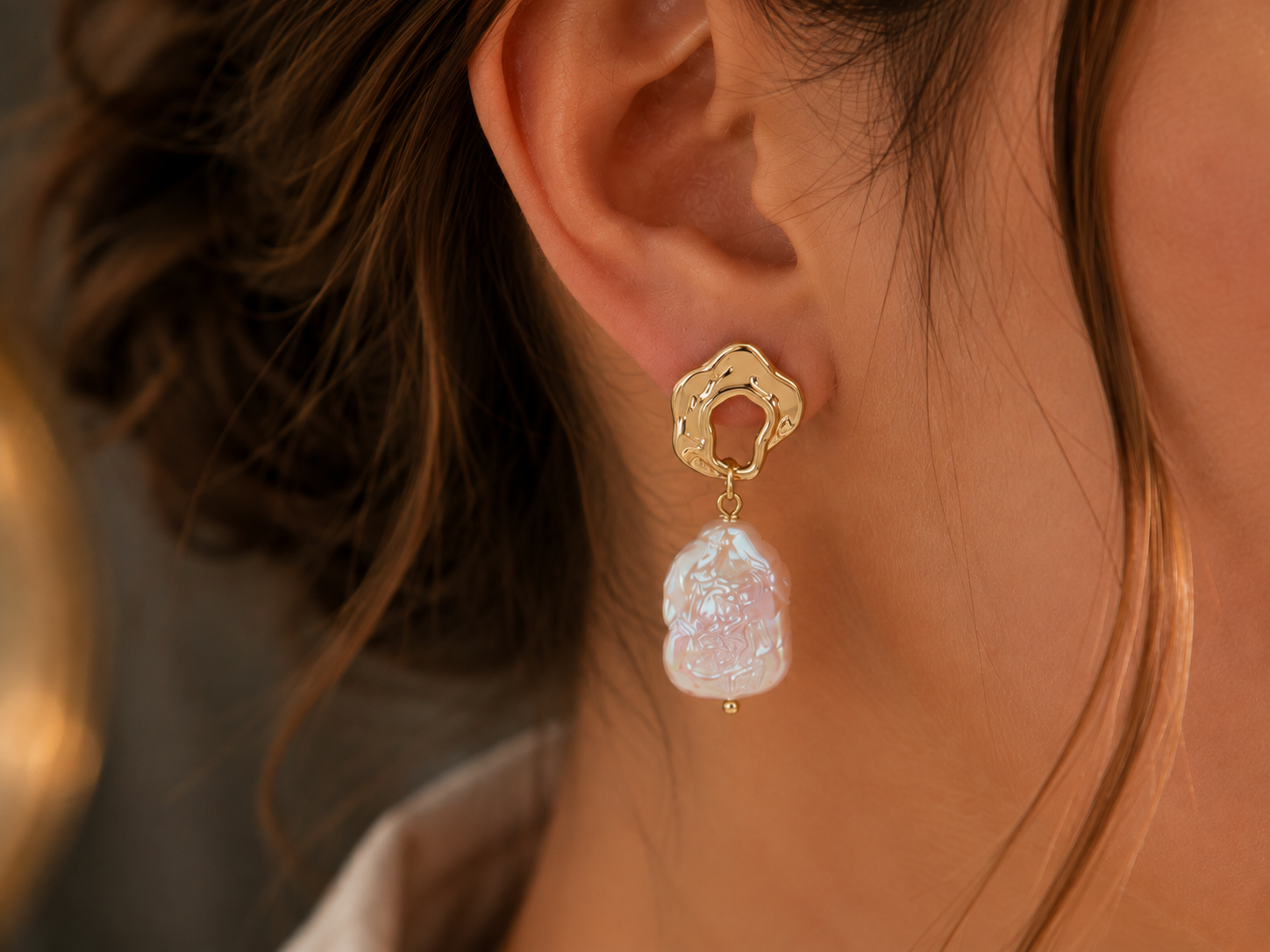 Close-up of a freshwater baroque pearl drop earring with a sculptural gold-tone stud