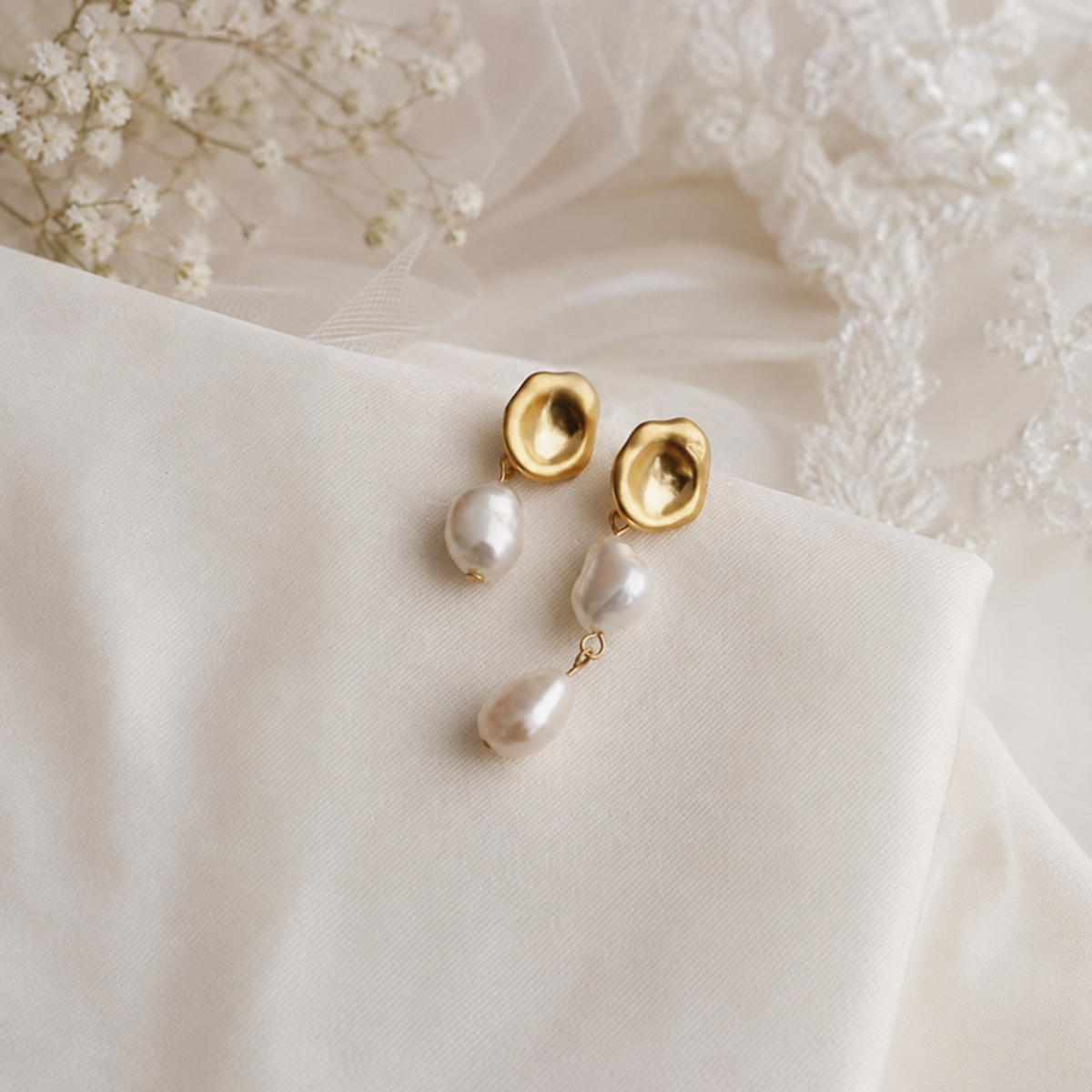 Asymmetric freshwater pearl drop earrings displayed on ivory bridal fabric