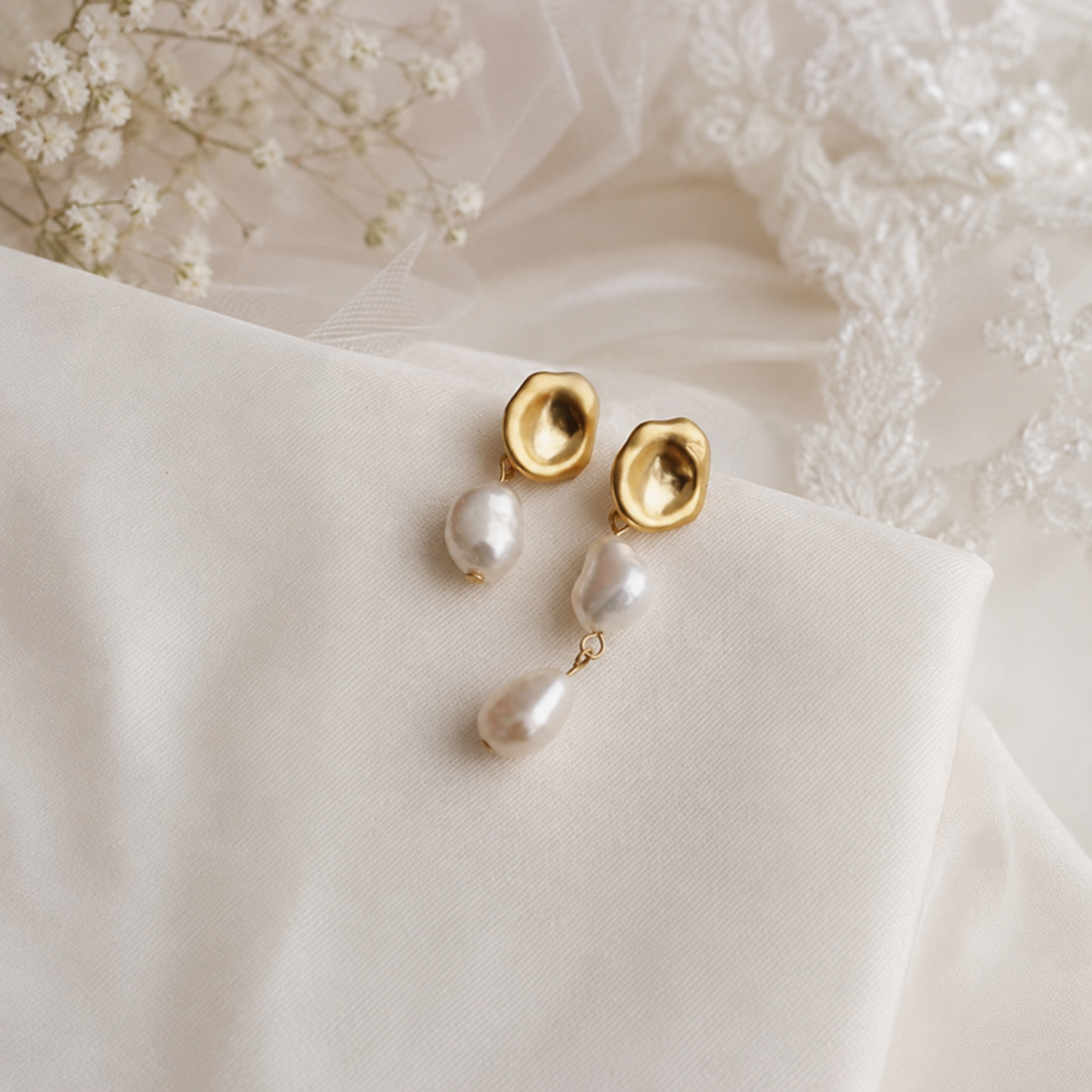 Asymmetric freshwater pearl drop earrings displayed on ivory bridal fabric