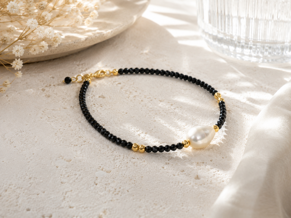 Close-up of a white freshwater pearl surrounded by black faceted beads and gold-tone details