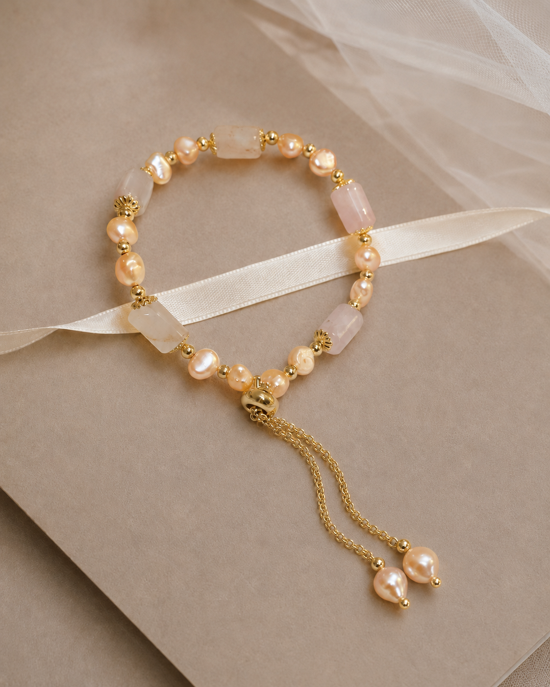 Champagne freshwater pearl bracelet with translucent blush beads and gold-tone details displayed with bridal fabric