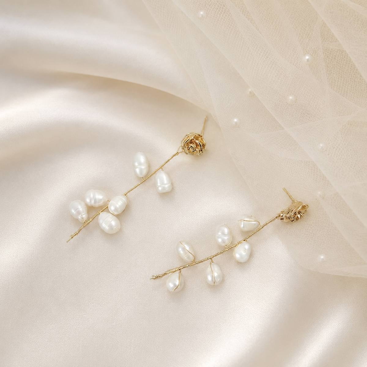Freshwater pearl rose vine drop earrings displayed on ivory satin beside a bridal veil