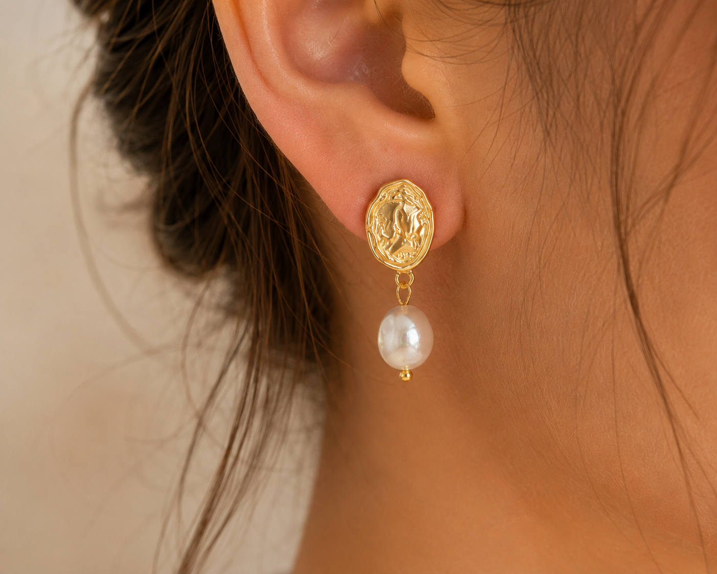 Close-up of a gold-tone vintage coin earring with a freshwater pearl drop