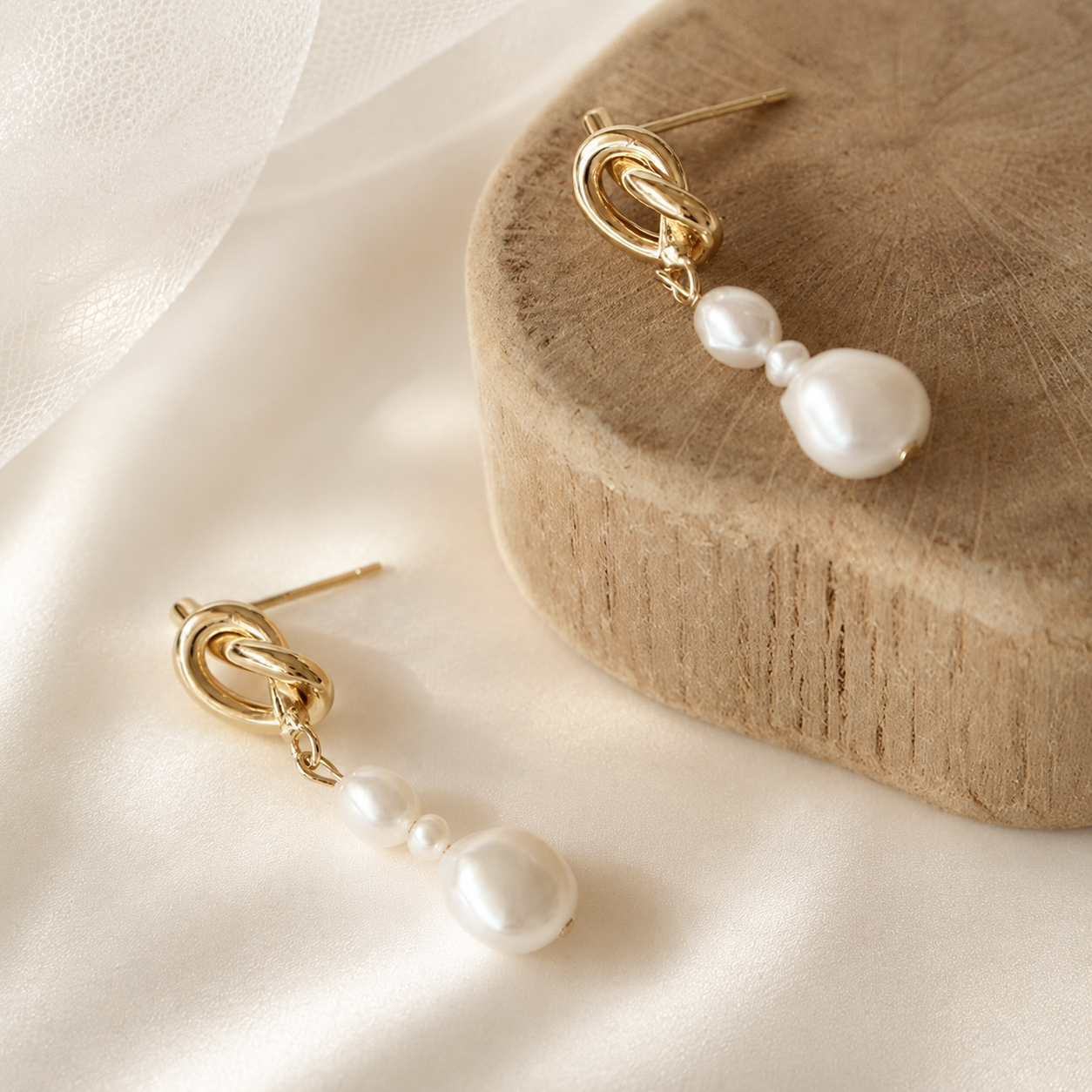 Close-up of white freshwater pearl drop earrings with polished gold knot studs