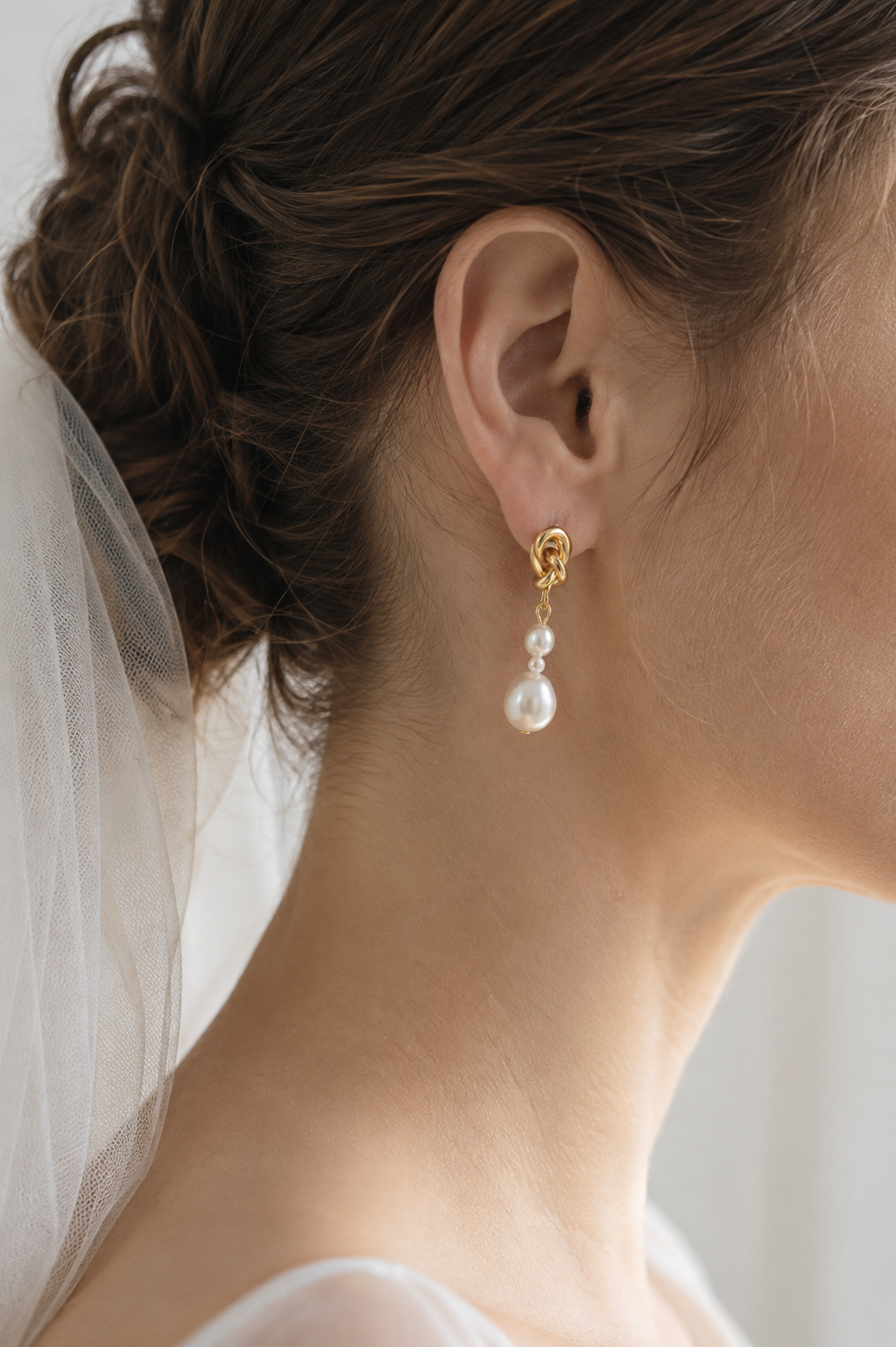 Side view of a bride wearing graduated white pearl and gold knot drop earrings