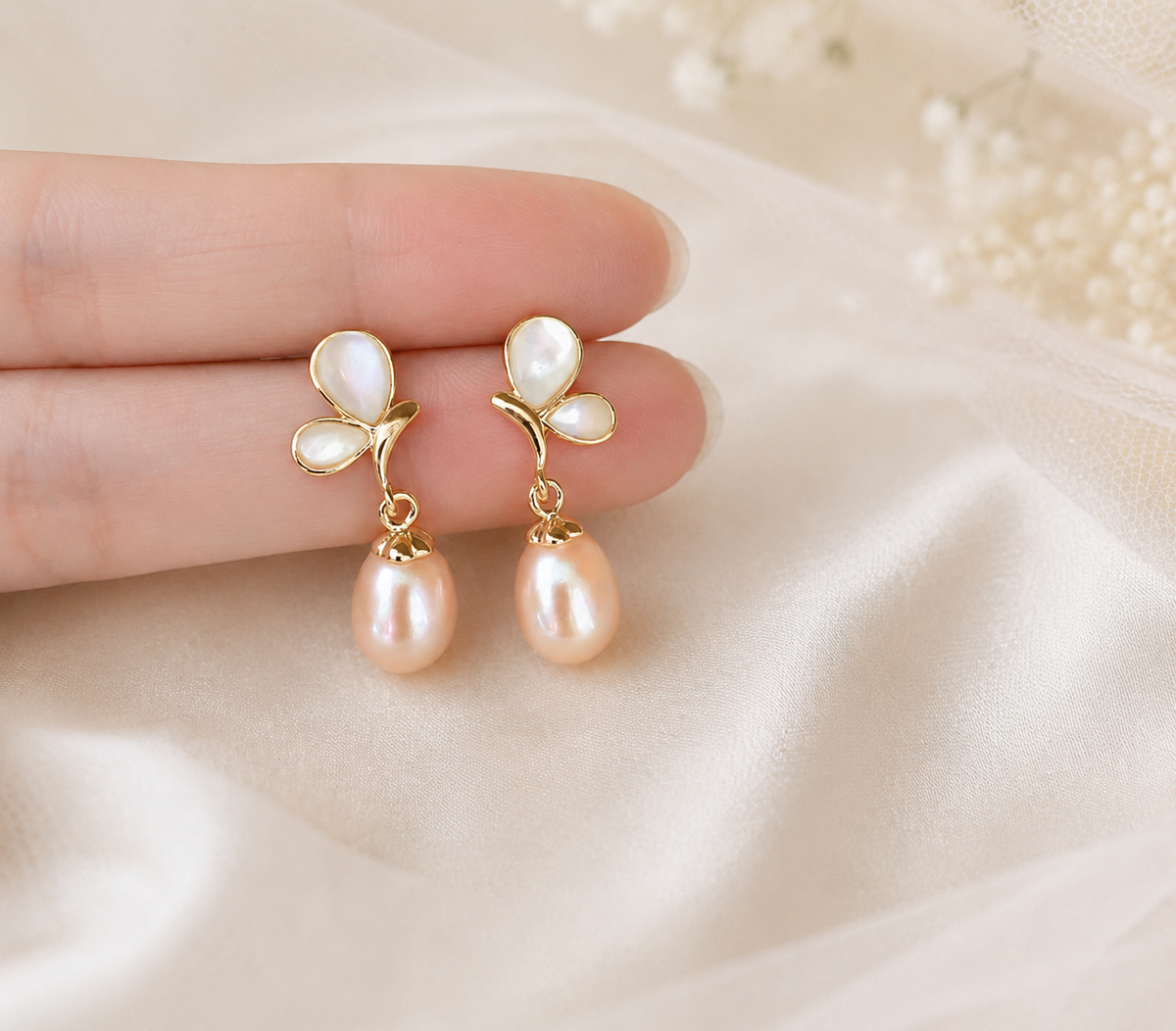 Pair of peach freshwater pearl and white butterfly earrings displayed in hand