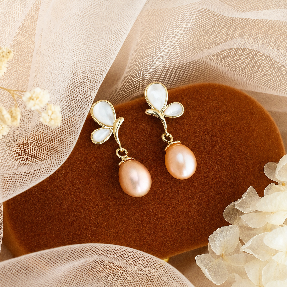Peach freshwater pearl butterfly earrings displayed on brown velvet