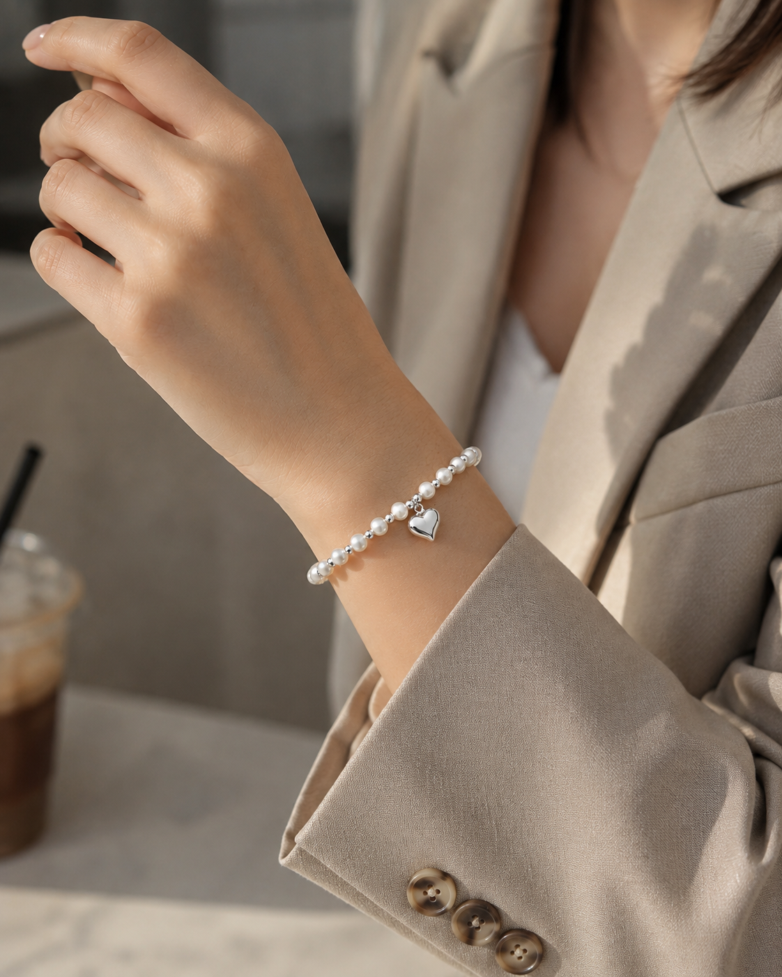 Woman styling a white pearl and silver-tone heart charm stretch bracelet with a blazer