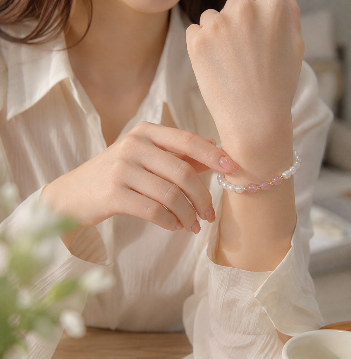 Woman wearing a pink bead and white pearl stretch bracelet with a white blouse