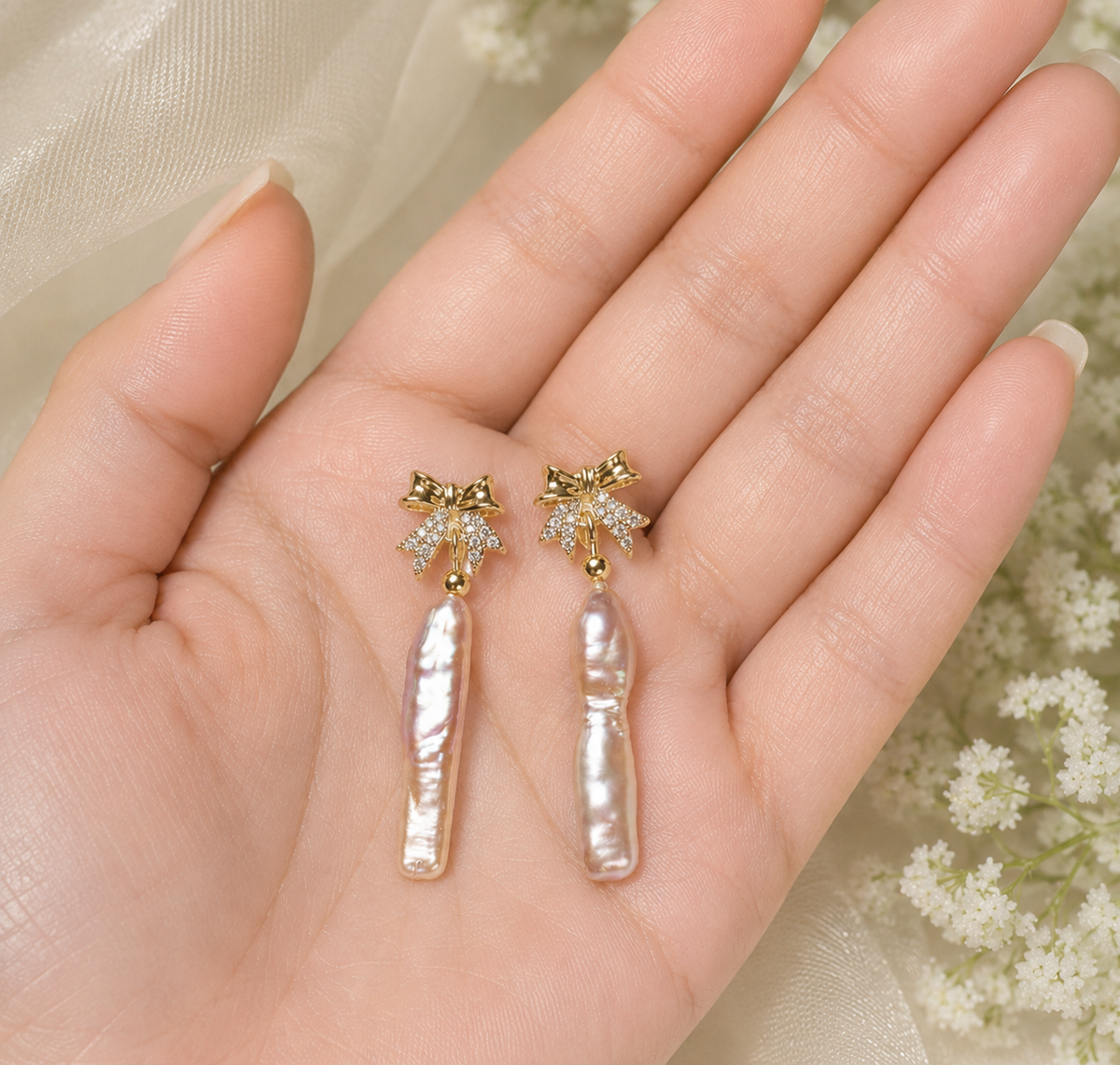 Long pink freshwater pearl earrings with sparkling gold-tone bows displayed in hand