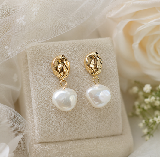 Sculptural gold stud earrings with large white baroque pearls on a bridal display