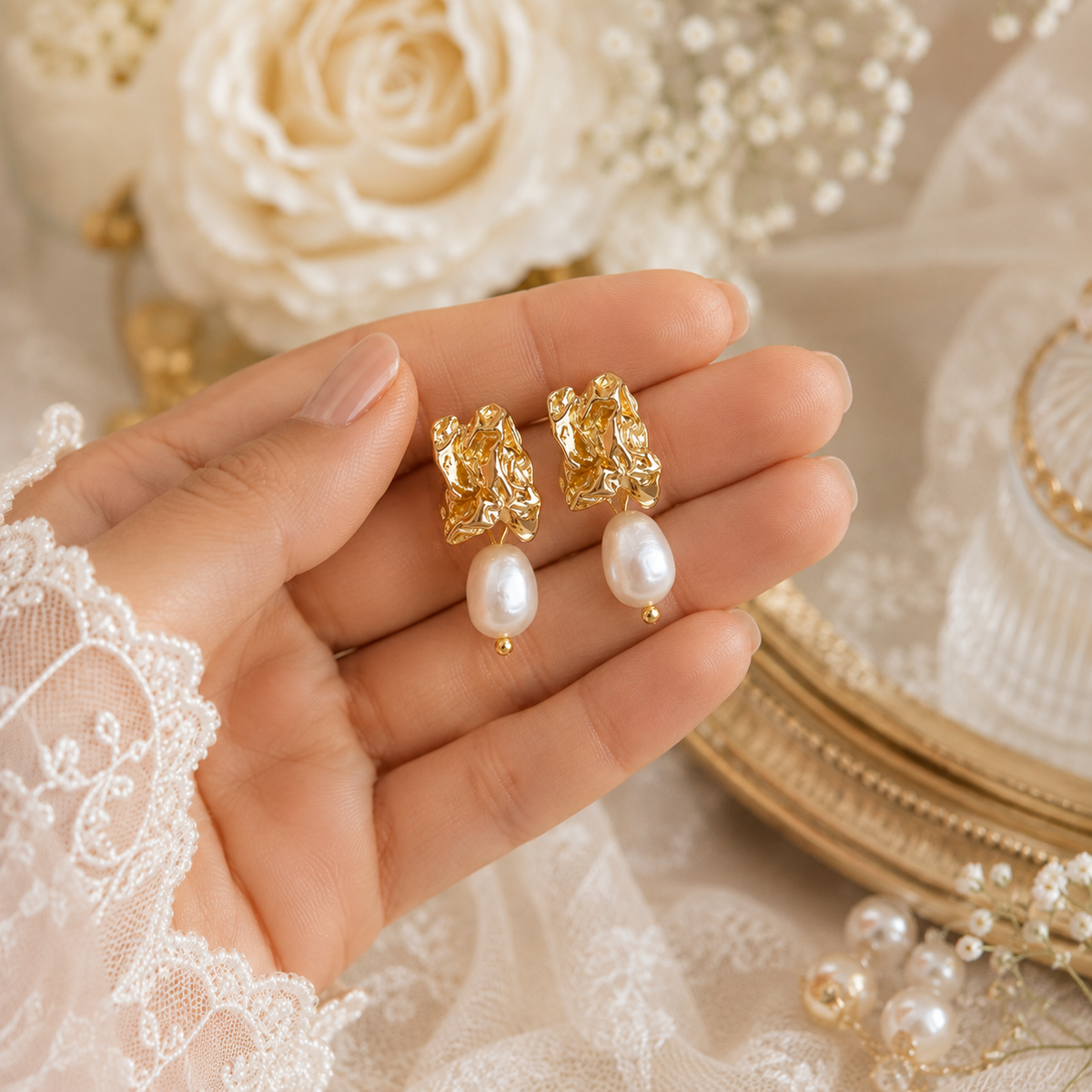 Pair of sculptural gold-tone earrings with white baroque pearls displayed in hand