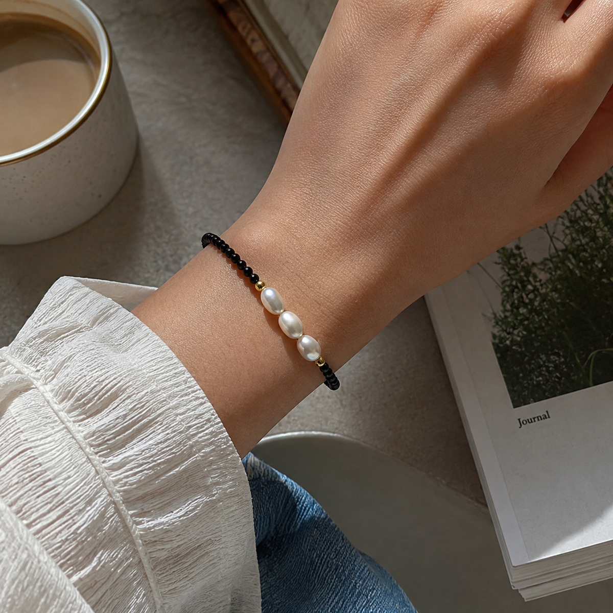 Triple freshwater pearl bracelet with black faceted beads and gold-tone accents worn on the wrist