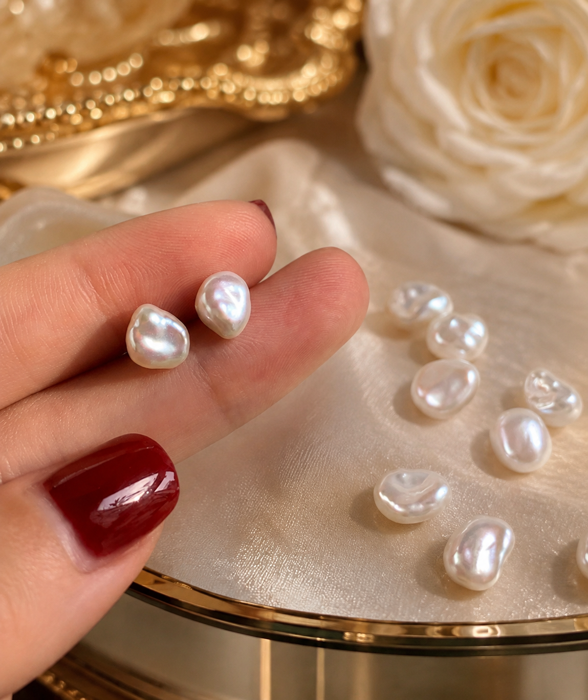 Pair of naturally irregular white baroque freshwater pearl stud earrings held on fingers