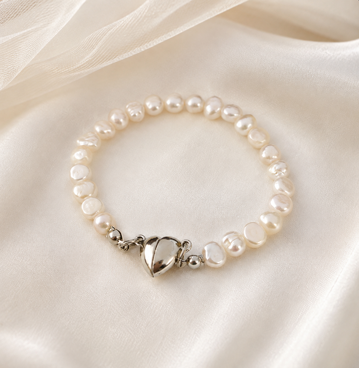 White baroque freshwater pearl bracelet with a silver-tone heart clasp displayed on satin