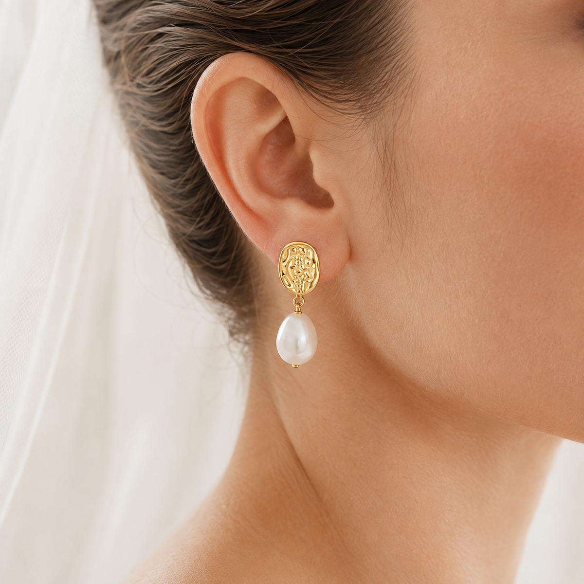 Close-up of a textured gold-tone drop earring with a white baroque freshwater pearl