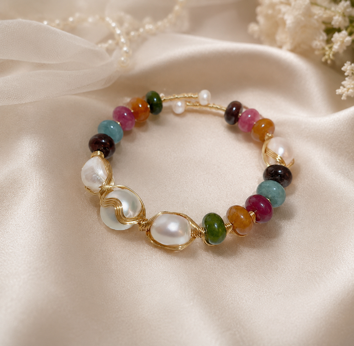 White baroque freshwater pearl bracelet with multicolor beads and gold-tone wire details displayed on champagne satin