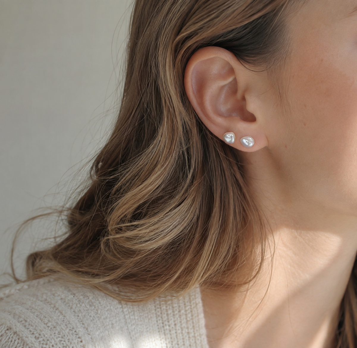 White baroque freshwater pearl stud earrings worn in a layered ear look