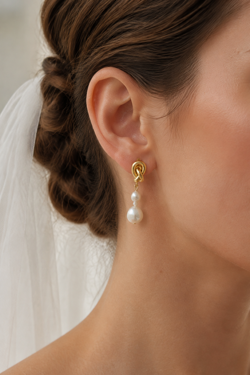 Close-up of a gold-tone knot earring with three graduated white freshwater pearls