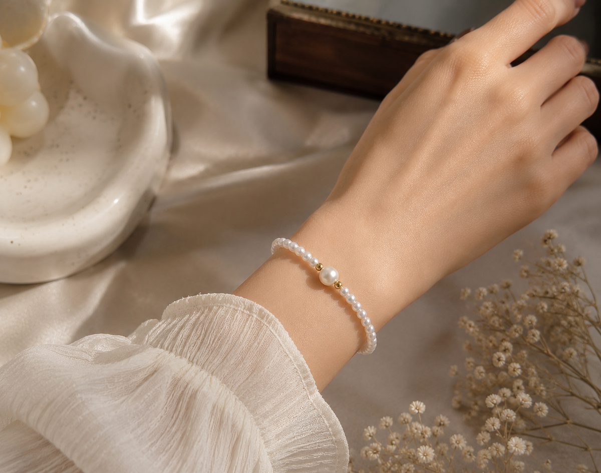 White pearl bracelet with a larger center pearl and two polished gold-tone beads worn on the wrist