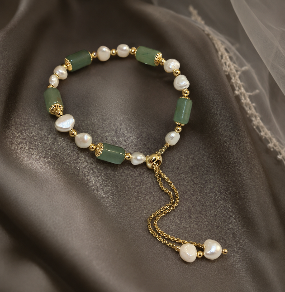 White freshwater pearl bracelet with rectangular green beads and an adjustable gold-tone closure displayed on dark satin