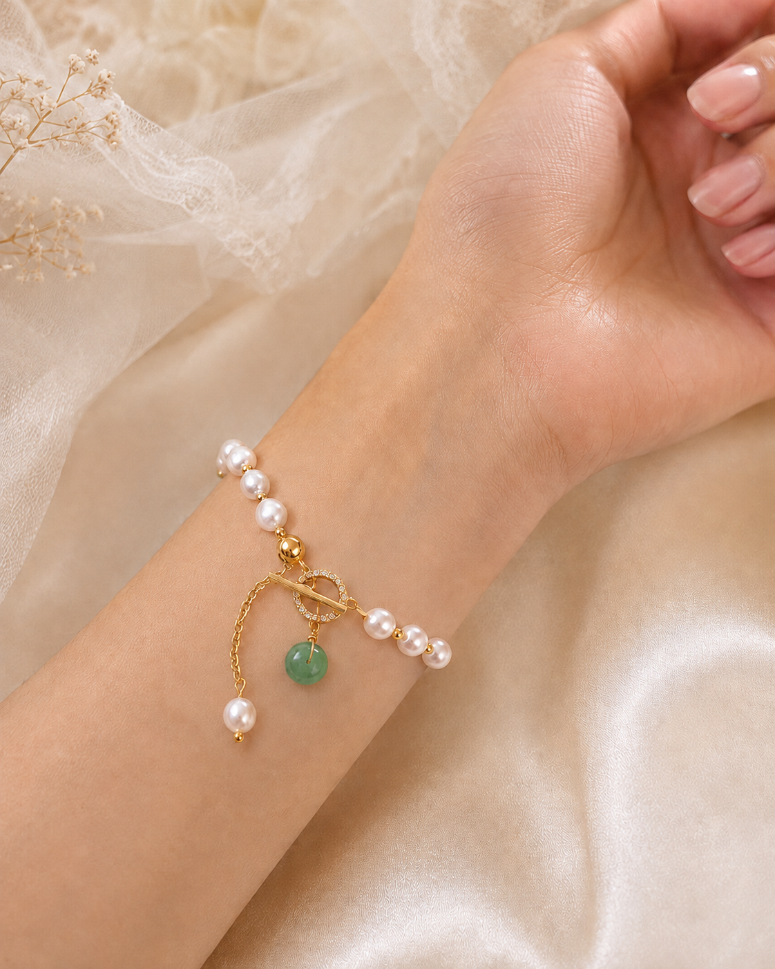 White freshwater pearl bracelet with green beads and a crystal-accented toggle closure worn on the wrist