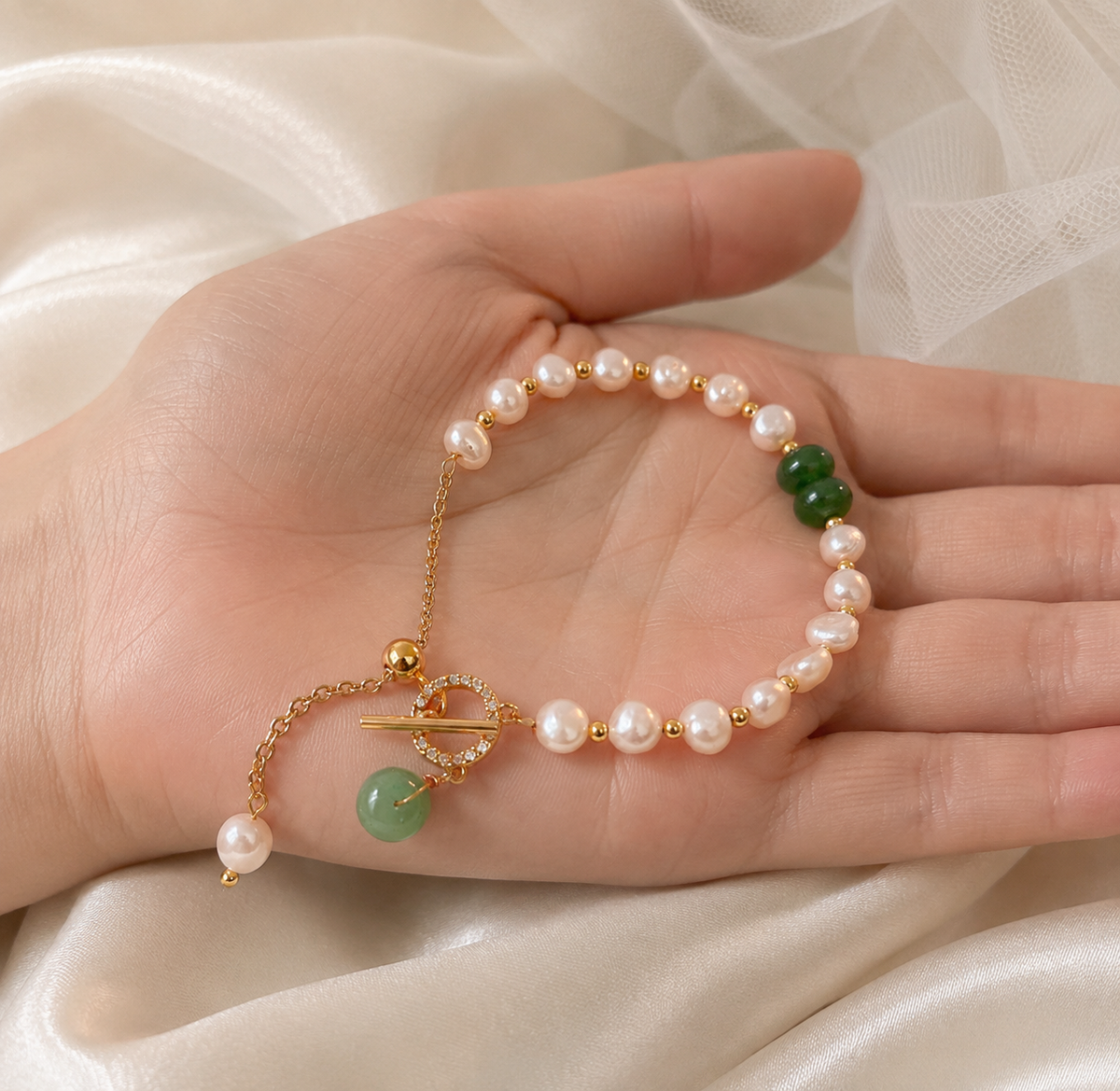 White freshwater pearl bracelet with green bead details and a gold-tone toggle closure displayed in hand