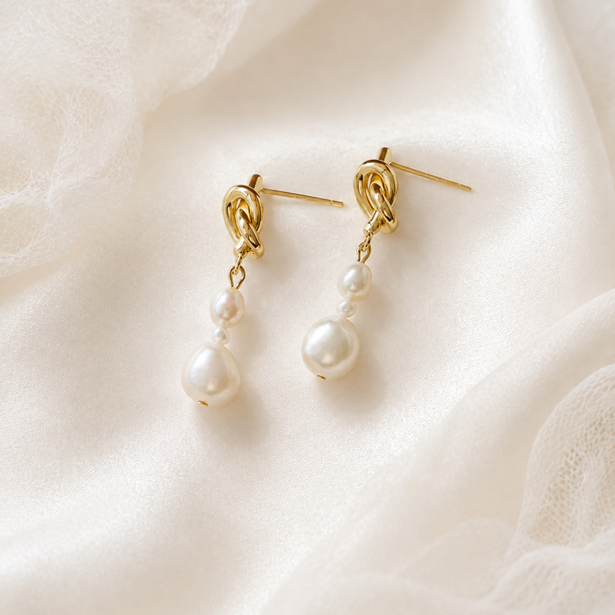 Pair of white freshwater pearl and gold knot drop earrings displayed on satin