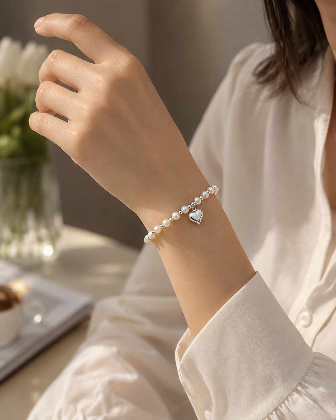 White pearl bracelet with alternating silver-tone beads and a heart charm worn on the wrist