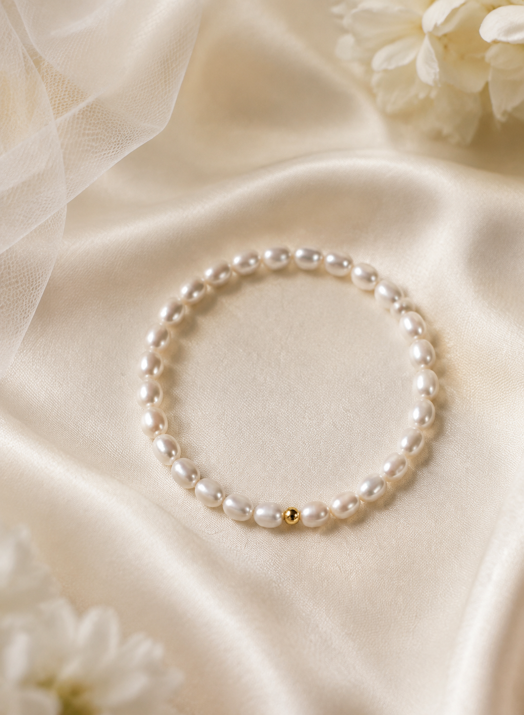 White rice freshwater pearl stretch bracelet with a single gold-tone accent bead displayed on satin